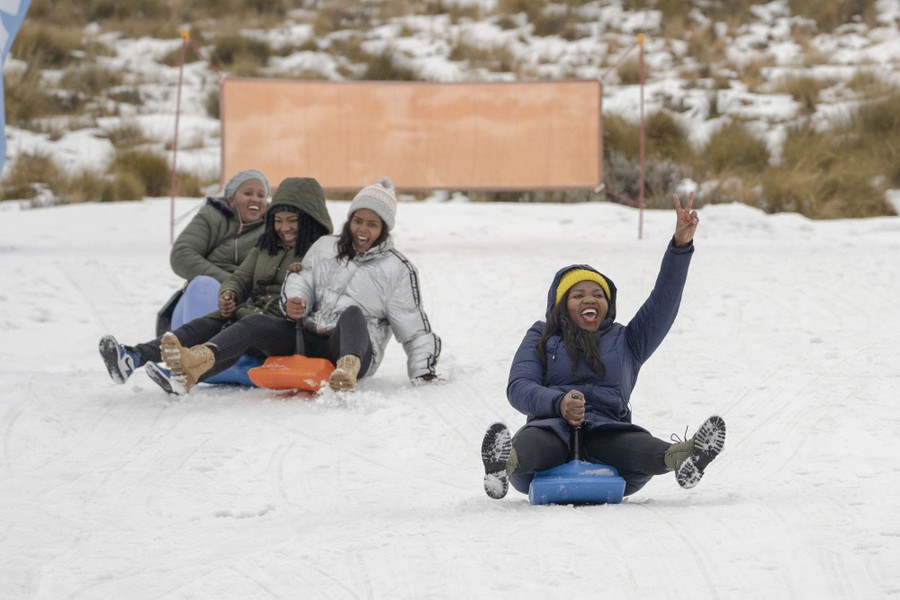 Several people sled down a snow-covered hill, laughing.