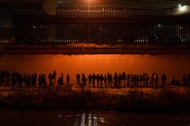 Migrants gathered at night in front of the border wall