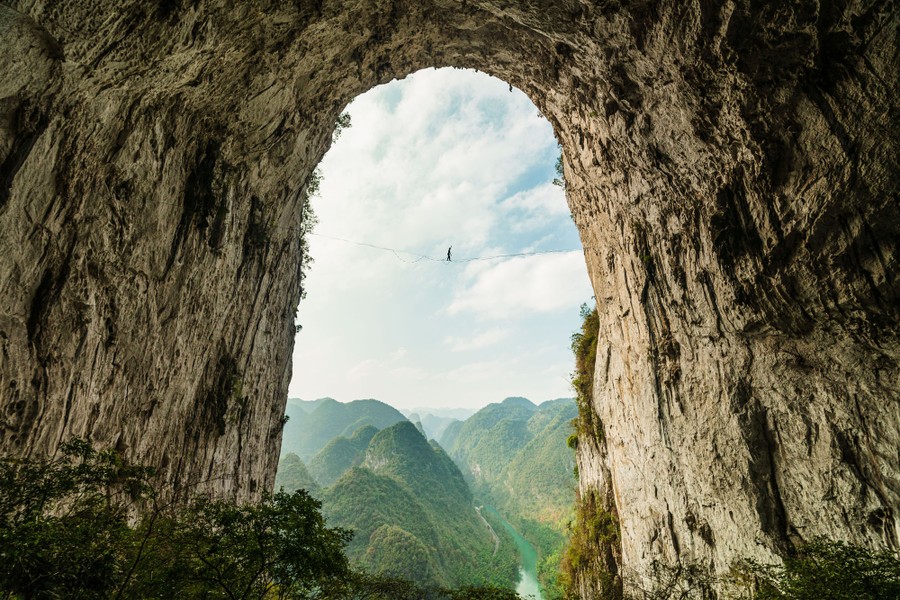 A slackliner walks a line inside an enormous natural archway in a mountain.