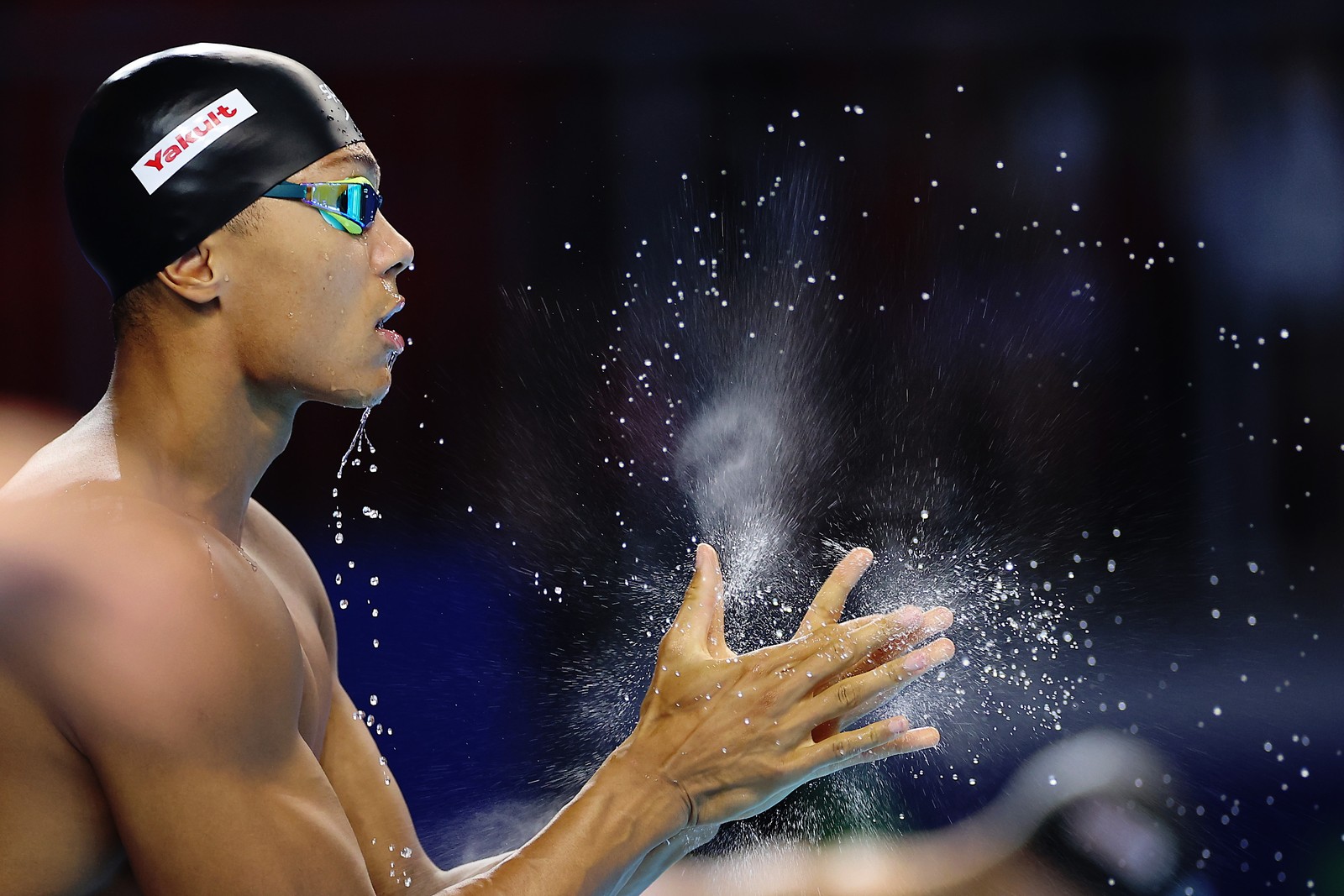 A swimmer, dripping wet, claps their hands, splashing water droplets everywhere.
