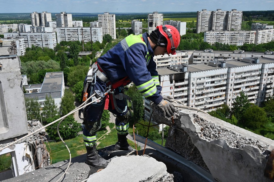 A worker stands on the roof of a tall apartment building, removing damaged pieces of the building.