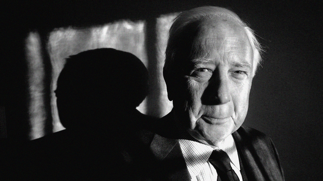 A black-and-white close-up photo of David McCullough from the shoulders up; he is wearing a suit and tie and smiling gently.