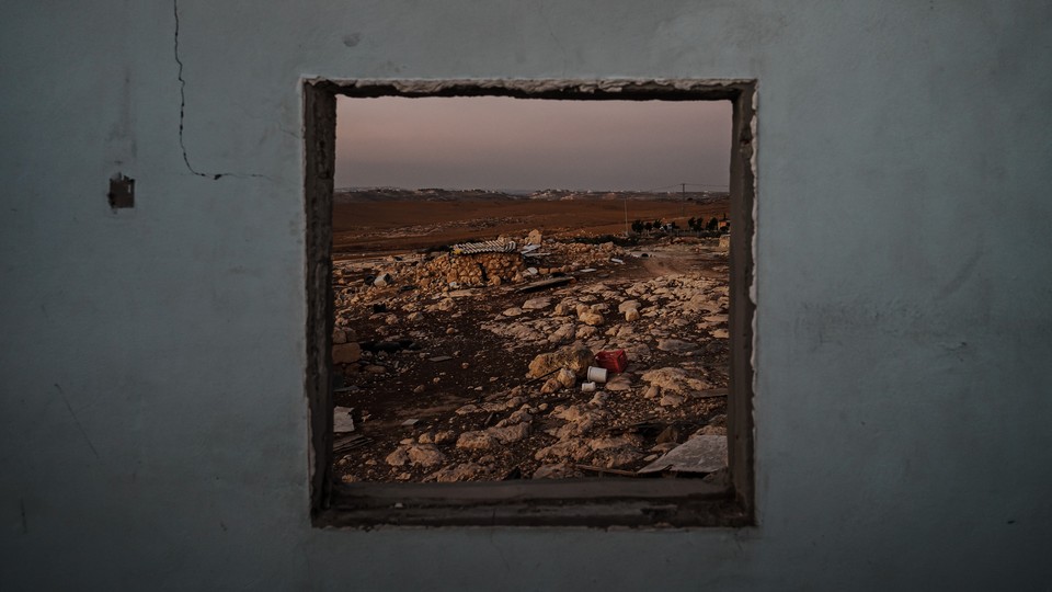 The wreckage of a neighborhood is framed by the empty window frame of an abandoned Palestinian home.