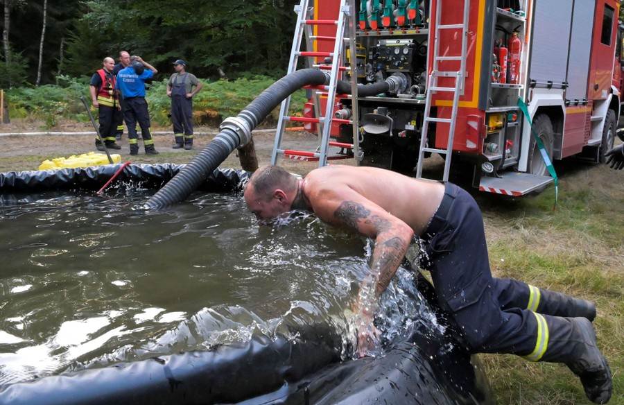 A firefighter leans over a temporary pool of water, splashing his face and upper body.