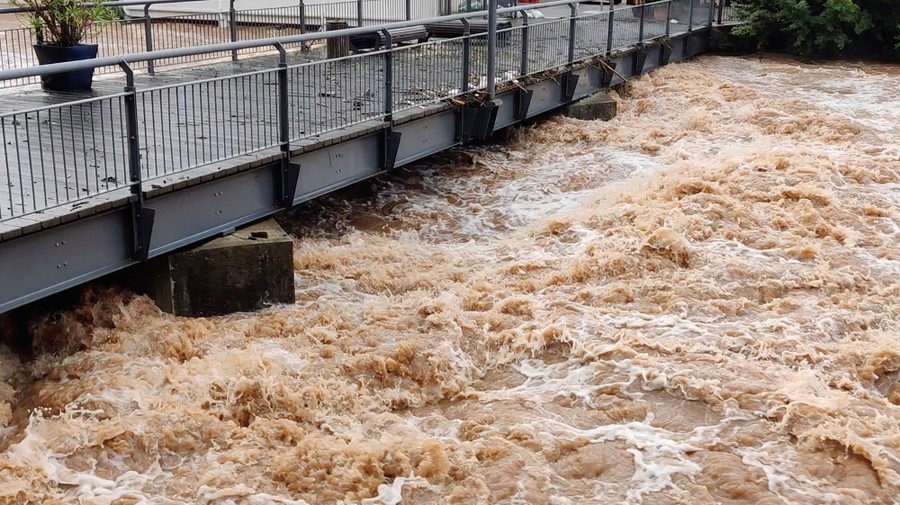 Floodwater runs under a pedestrian bridge.