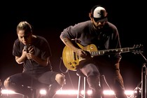 Lady Gaga at the Oscars, wearing a black T-shirt and ripped jeans, sitting on a stool to perform a stripped-down version of 'Hold My Hand,' from 'Top Gun: Maverick'