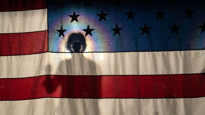Elizabeth Warren's silhouette is illuminated behind an American flag