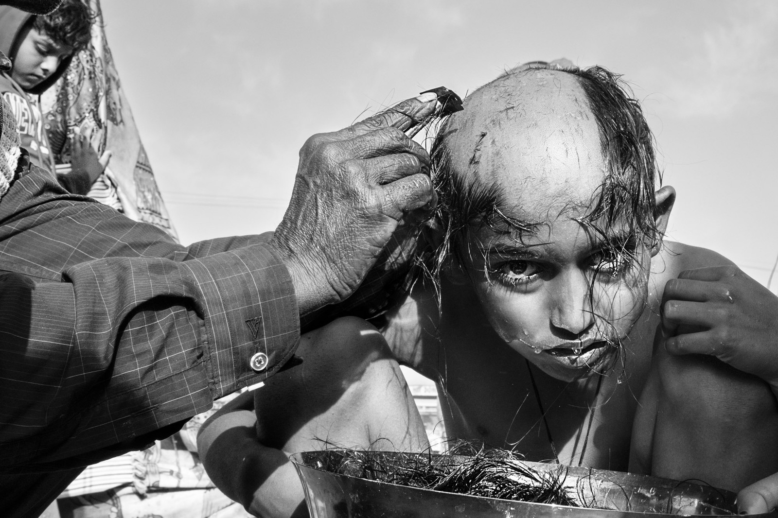 A boy looks toward the camera while his head is being shaved with a razor.