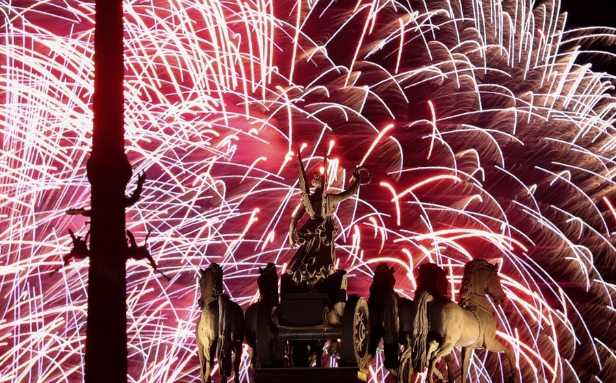 Fireworks explode in the sky above a statue of horses and a chariot.