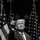 Black-and-white photograph of Donald Trump in front of some American flags