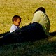 A father and small child relax on the grass.