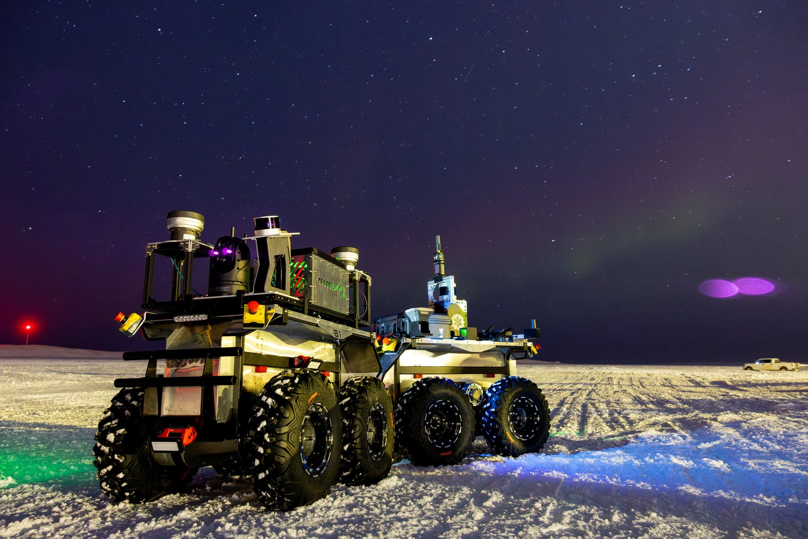An autonomous eight-wheeled robot sits on a snow-covered plain at night.