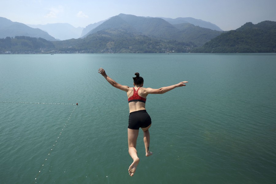 A person jumps into a mountain lake from a high perch.