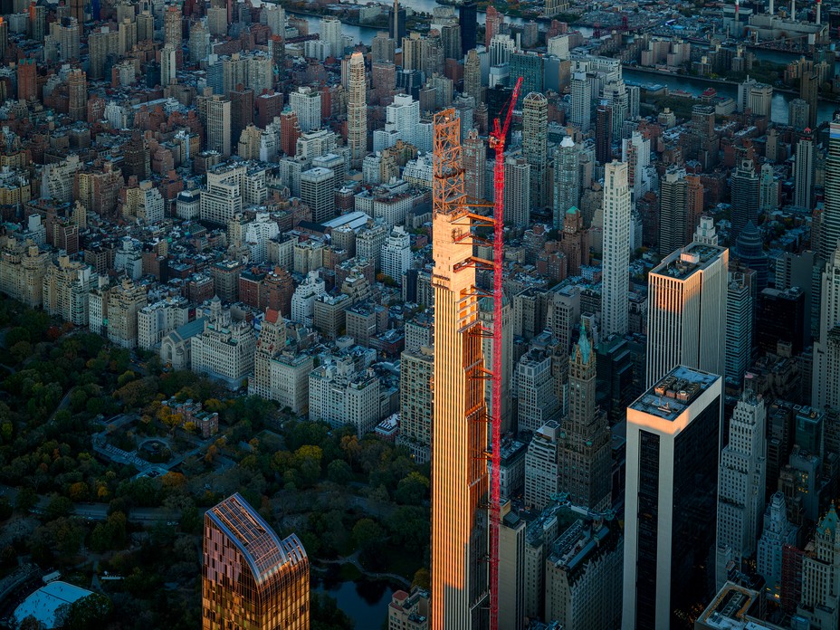 photo of supertall building under construction with red crane attached at multiple points and Central Park far below