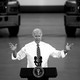A black-and-white photo of Joe Biden speaking at a podium in front of two trucks.