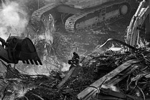 Photo of firefighter sitting on twisted metal wreckage surrounded by enormous excavators