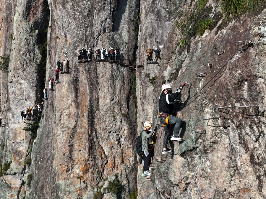 Tourists navigate the face of a cliff, moving along narrow platforms and steps.