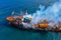 A severely damaged and smoking cargo ship is seen at sea.
