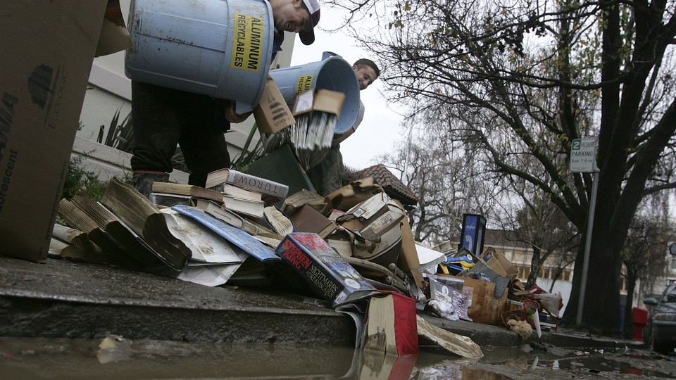 Workers dump recycling bins full of books and magazines on the ground.