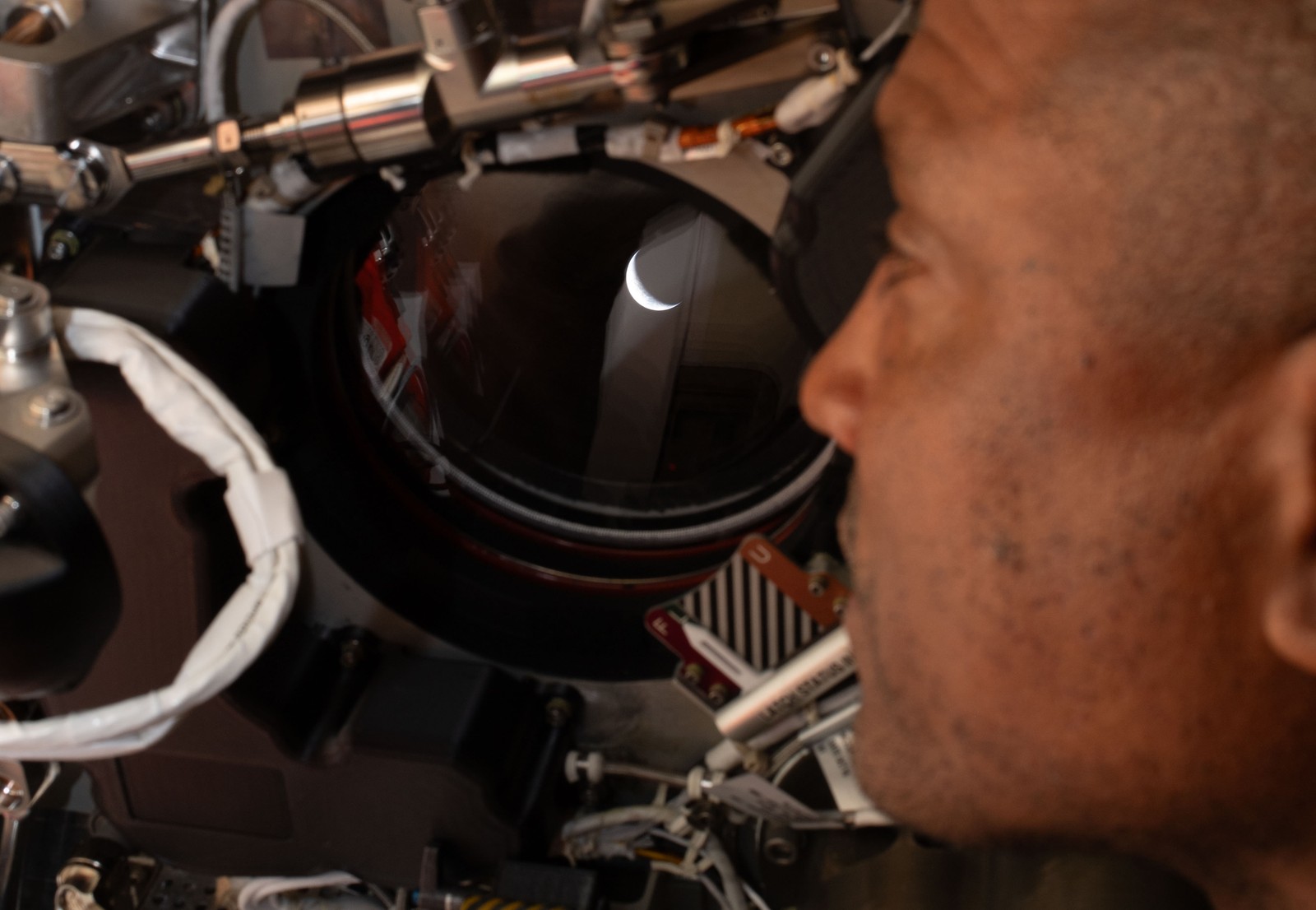 Artemis II pilot and NASA astronaut Victor Glover peers out one of the Orion spacecraft’s windows, looking back at Earth.
