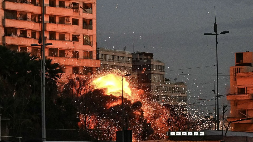 Photograph of flames bursting from an explosion on the side of a building at dusk