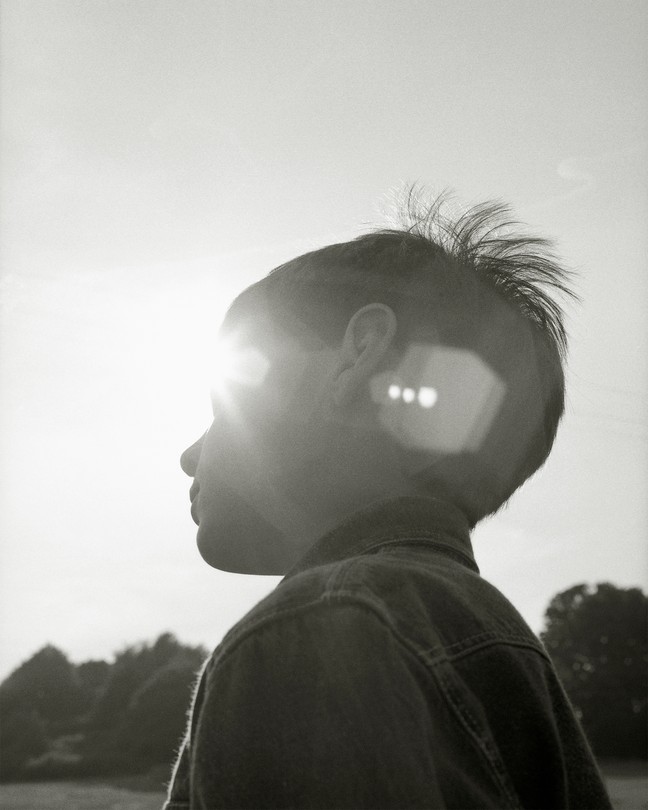 a young boy looking ahead, his face partially covered by the glare of the sun