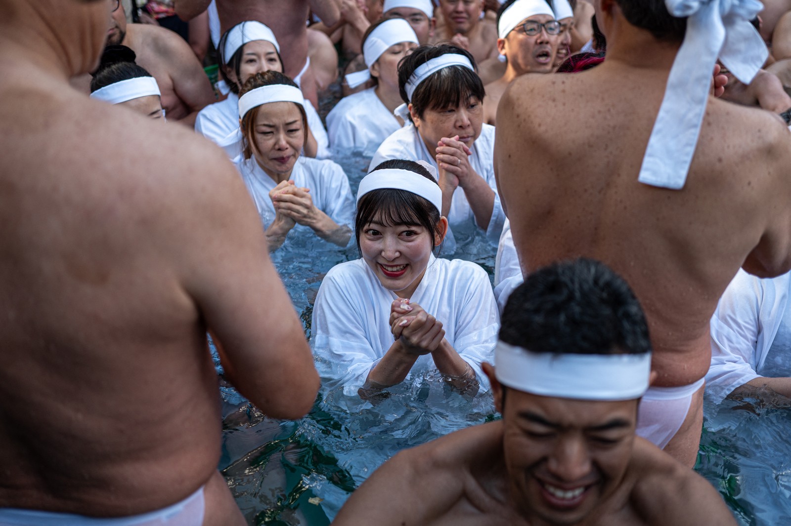 A group of people wearing traditional white clothing and headbands take a ritual dip in a large ice bath.