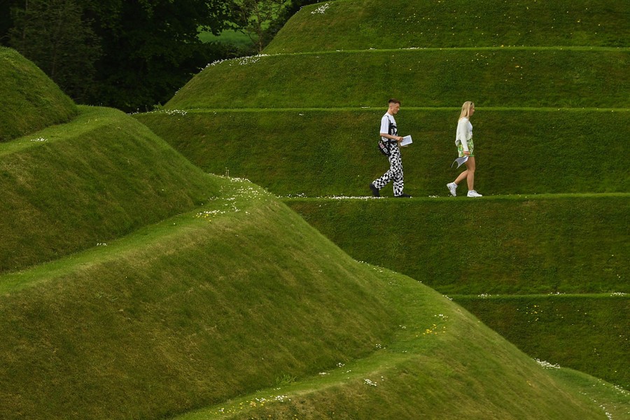 People walk on a terraced hillside covered in short grass.