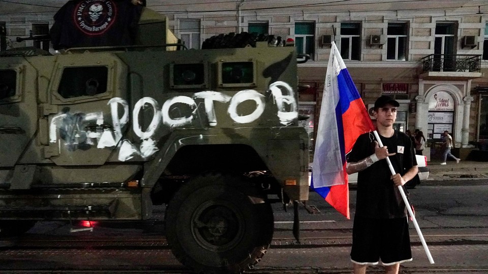Photograph of a man holding aRussian flag next to an army tank