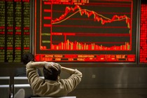 An investor holds his head in front of a red screen with fluctuating stock prices
