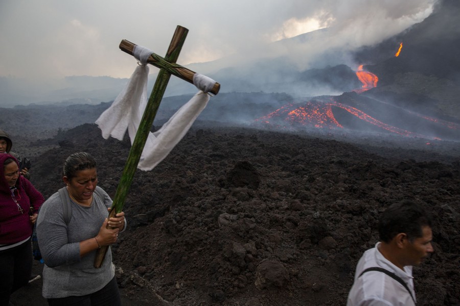 A woman carries a cross near a lava flow.