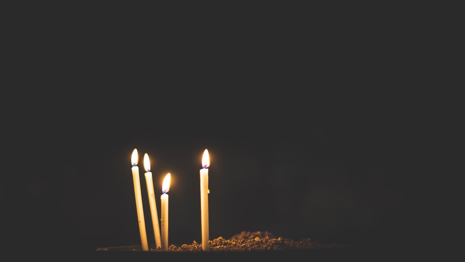 Four candles burn against a dark backdrop.