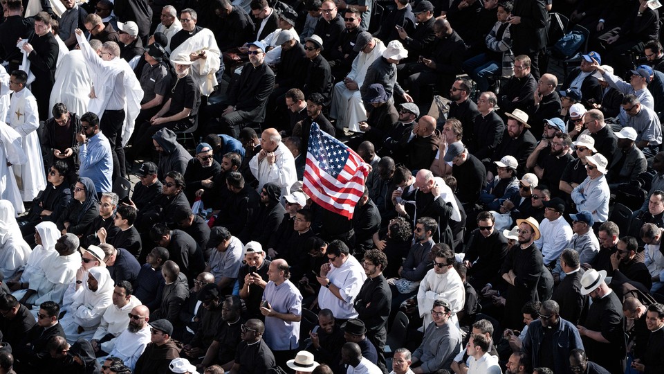 In a crowd of Catholics, one holds up an American flag