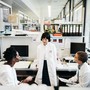 Three people in lab coats converse in a lab space with computers.