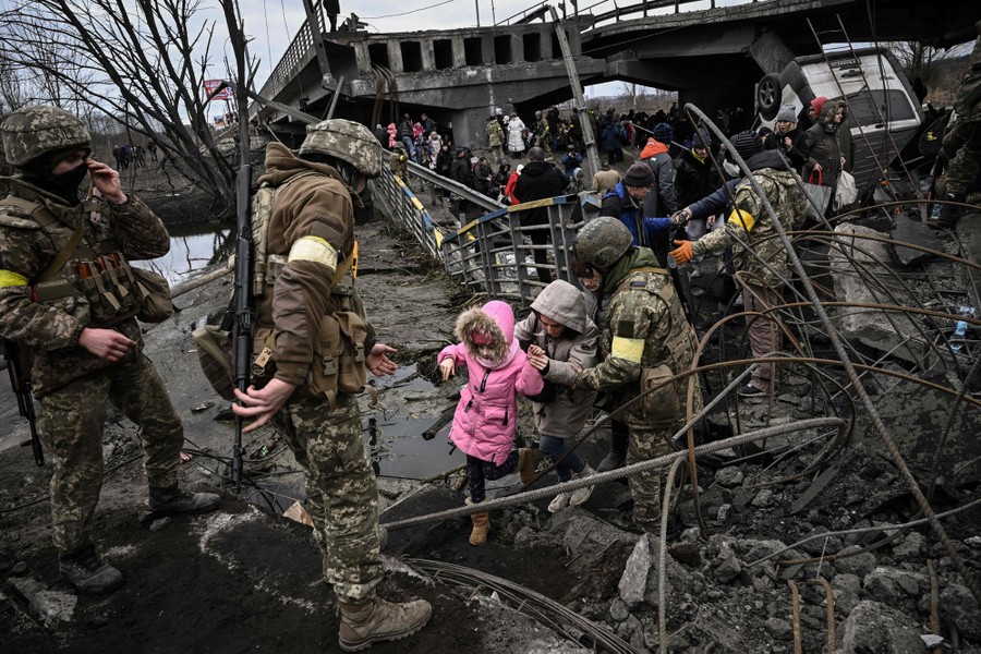 Soldiers help civilians walk across the remains of a destroyed bridge.