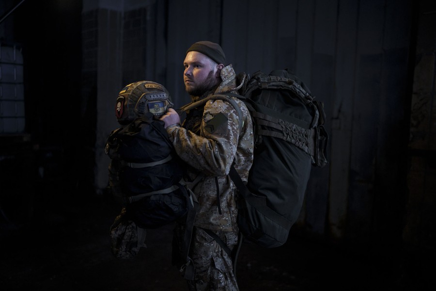 A portrait of a soldier carrying large bags of gear and his helmet