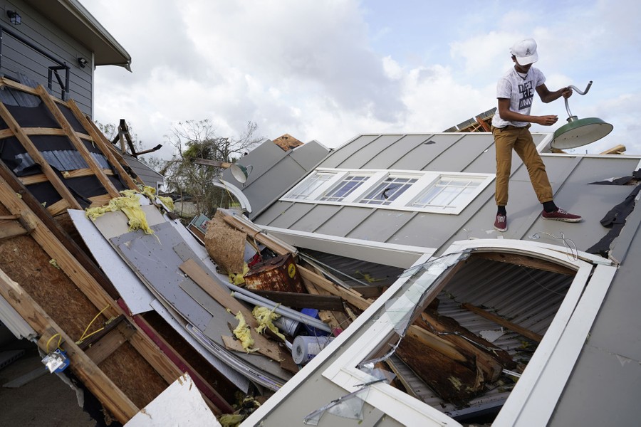 A person stands on top the rubble of a destroyed storage unit holding a light fixture.