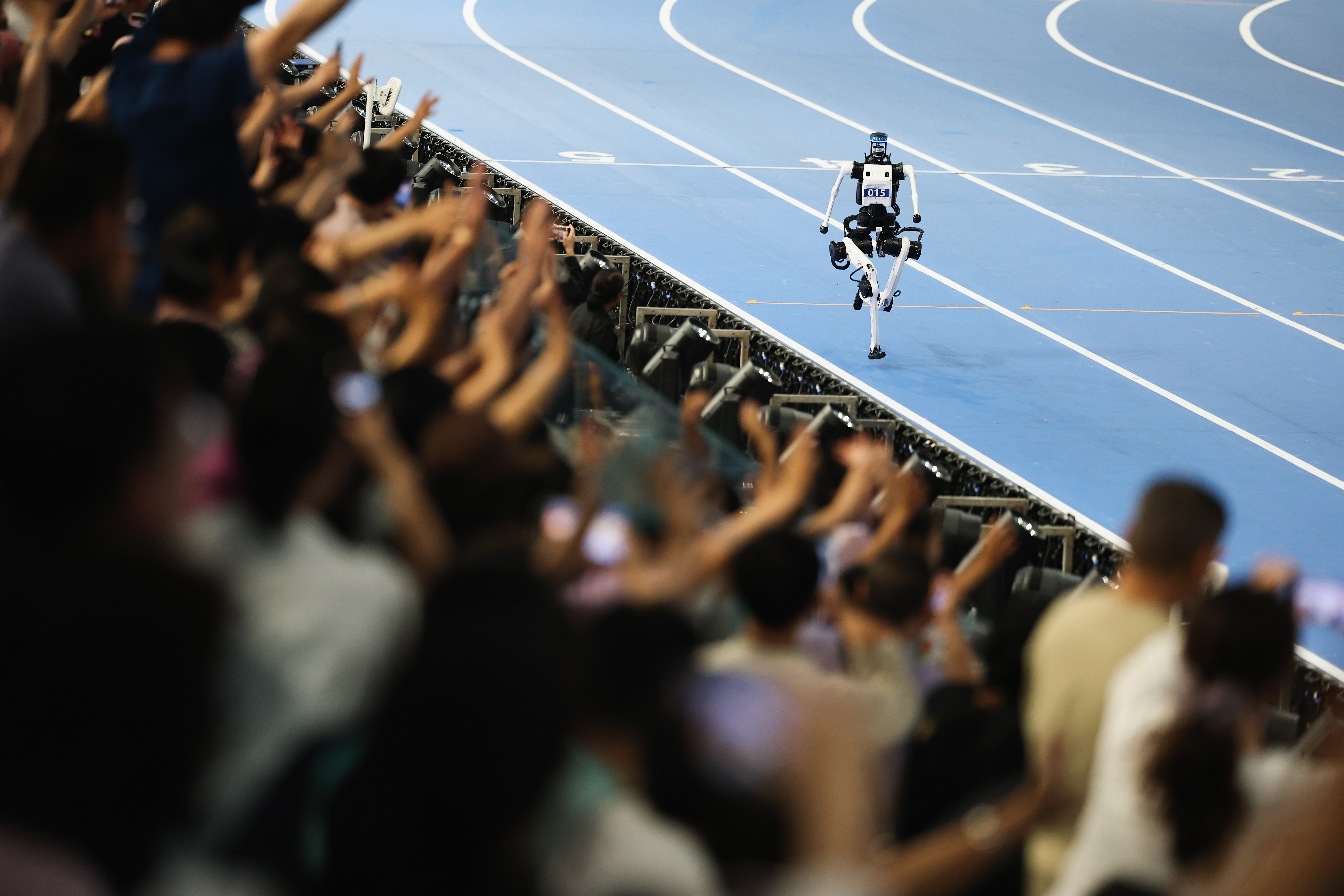 A crowd cheers as a humanoid robot runs past them on a track.