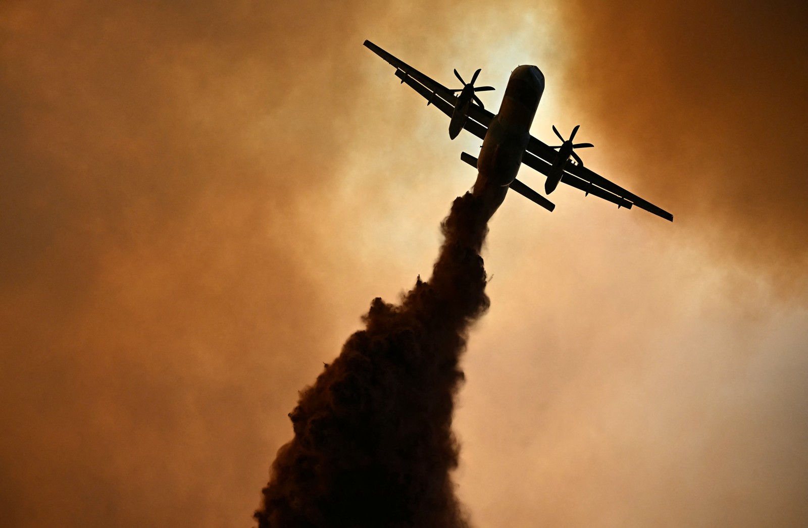 A firefighting aircraft drops a plume of fire retardant.
