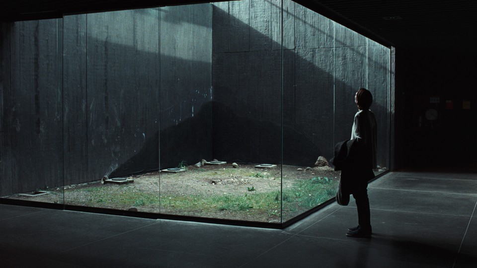 Tilda Swinton standing before a glass room in "Memoria"