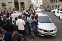 Uber taxi drivers in South Africa stand near their cars and block a road during a protest