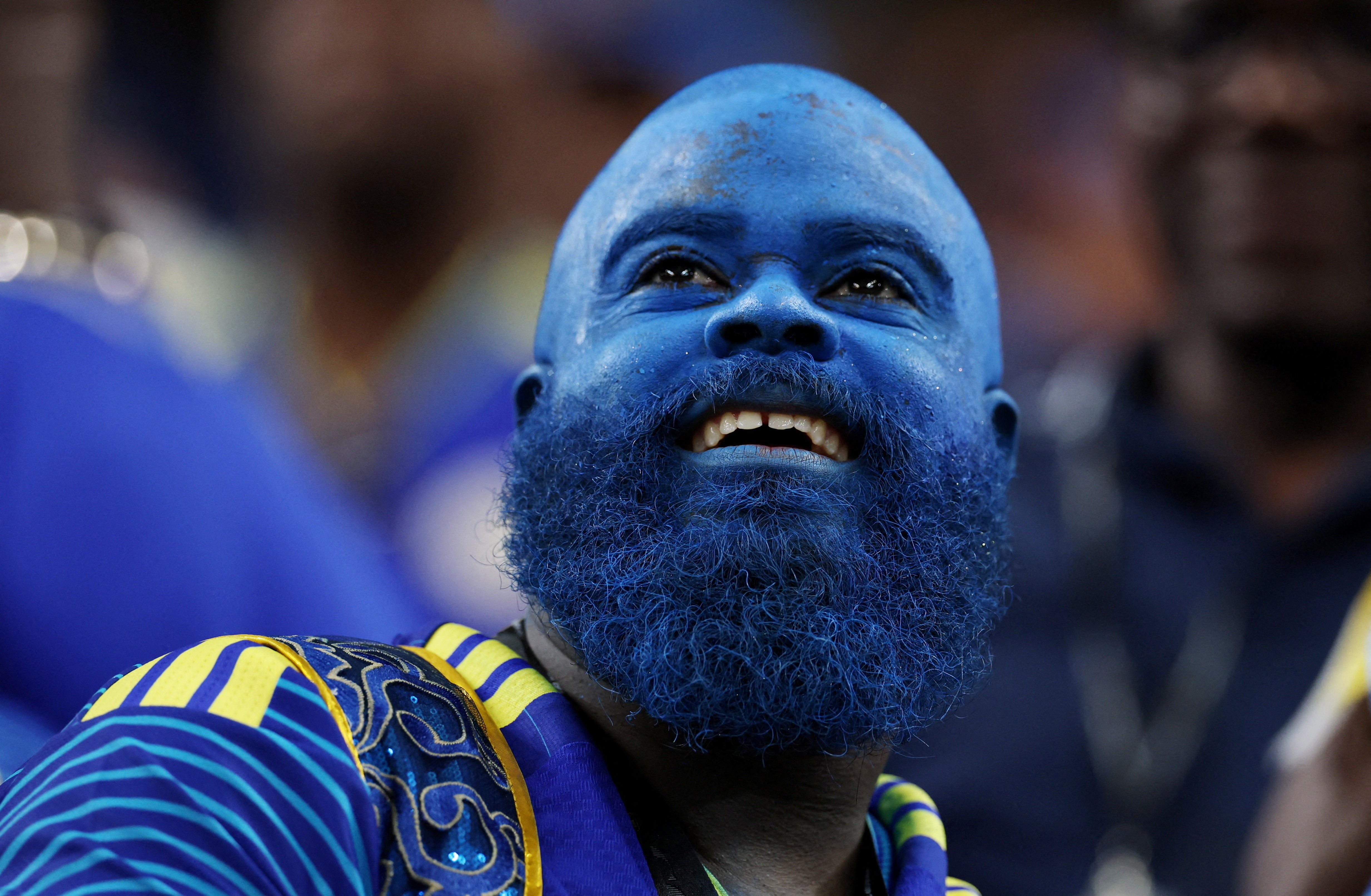 A soccer fan, their entire head, face, and beard covered in blue makeup