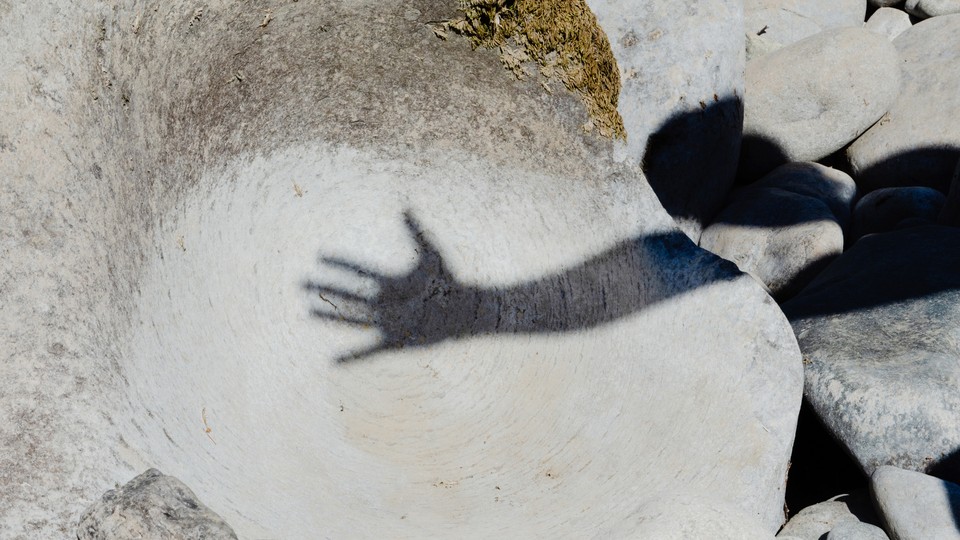 a shadow of someone raising a hand and spreading their fingers apart on a big grey rock