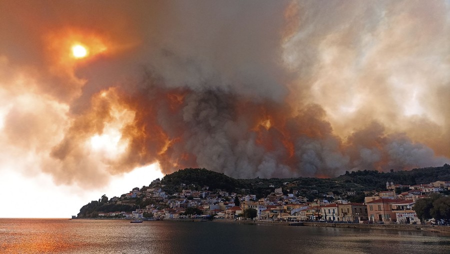 Smoke and flames rise above a coastal Greek village.