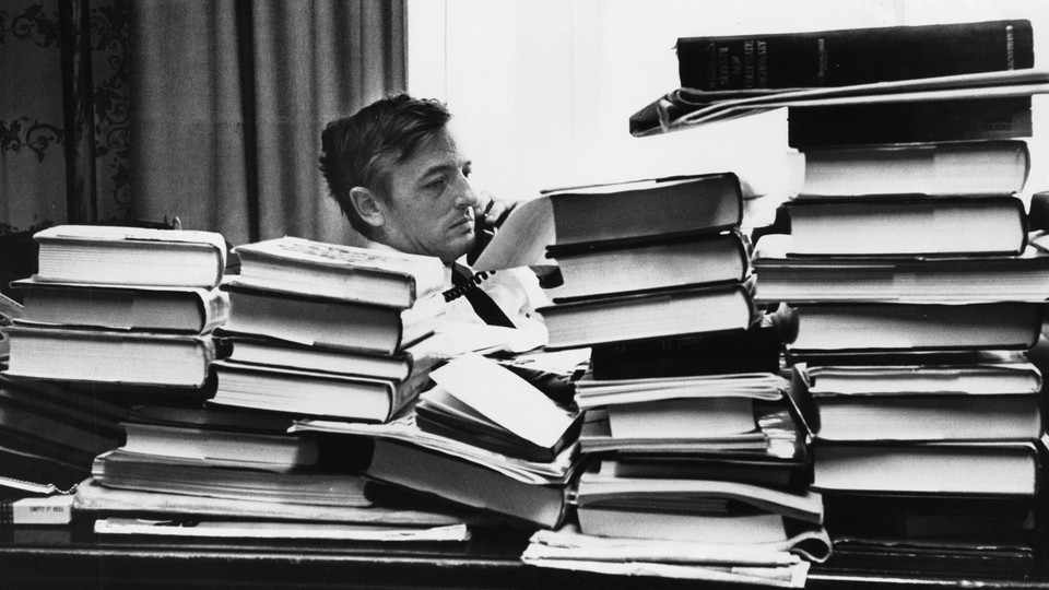 a black and white photo of William F. Buckley sitting at a desk surrounded by books