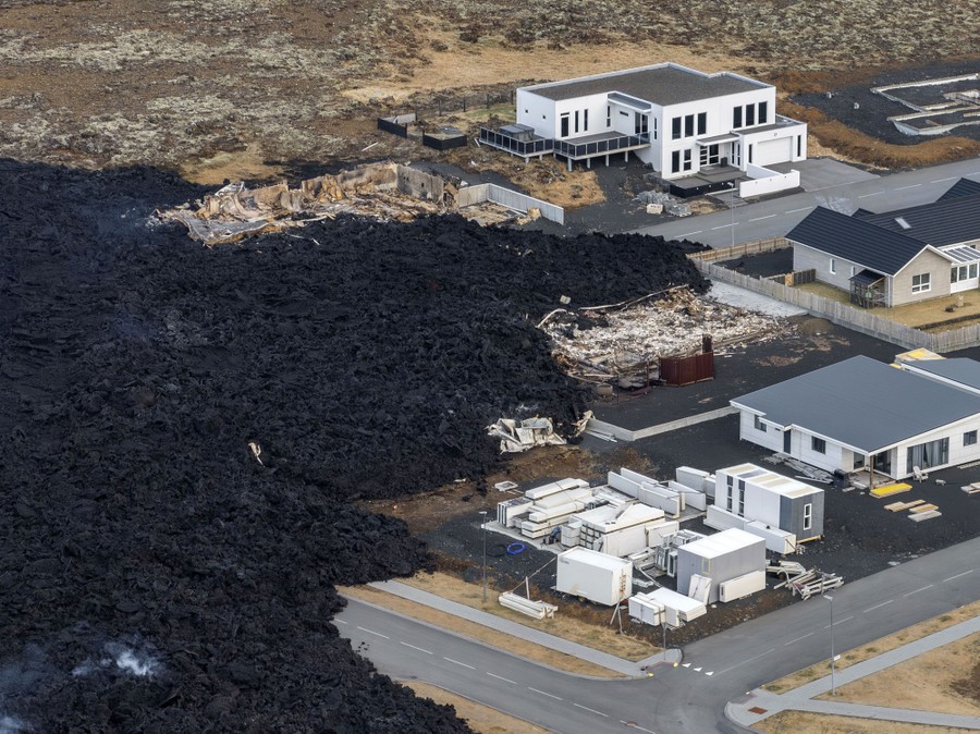 An aerial view of a cooling lava flow amid a residential area, with several burned houses