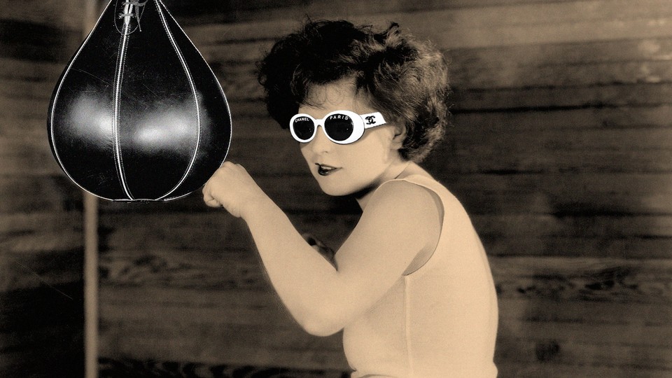 A woman in "clout goggles" (white sunglasses) hits a punching bag.
