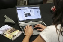 A photo taken over someone's shoulder of an open laptop screen, which displays a Facebook News Feed