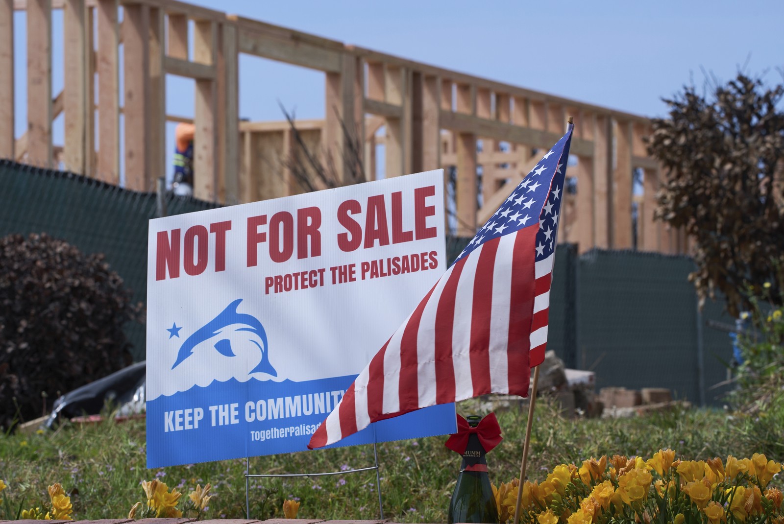 An American flag and a sign stand in front of a house under construction. The sign reads