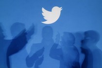 The shadows of people using smartphones against a blue backdrop with the Twitter logo